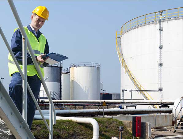 imagen de un hombre con casco y chaleco, de fondo infraestructura industrial 